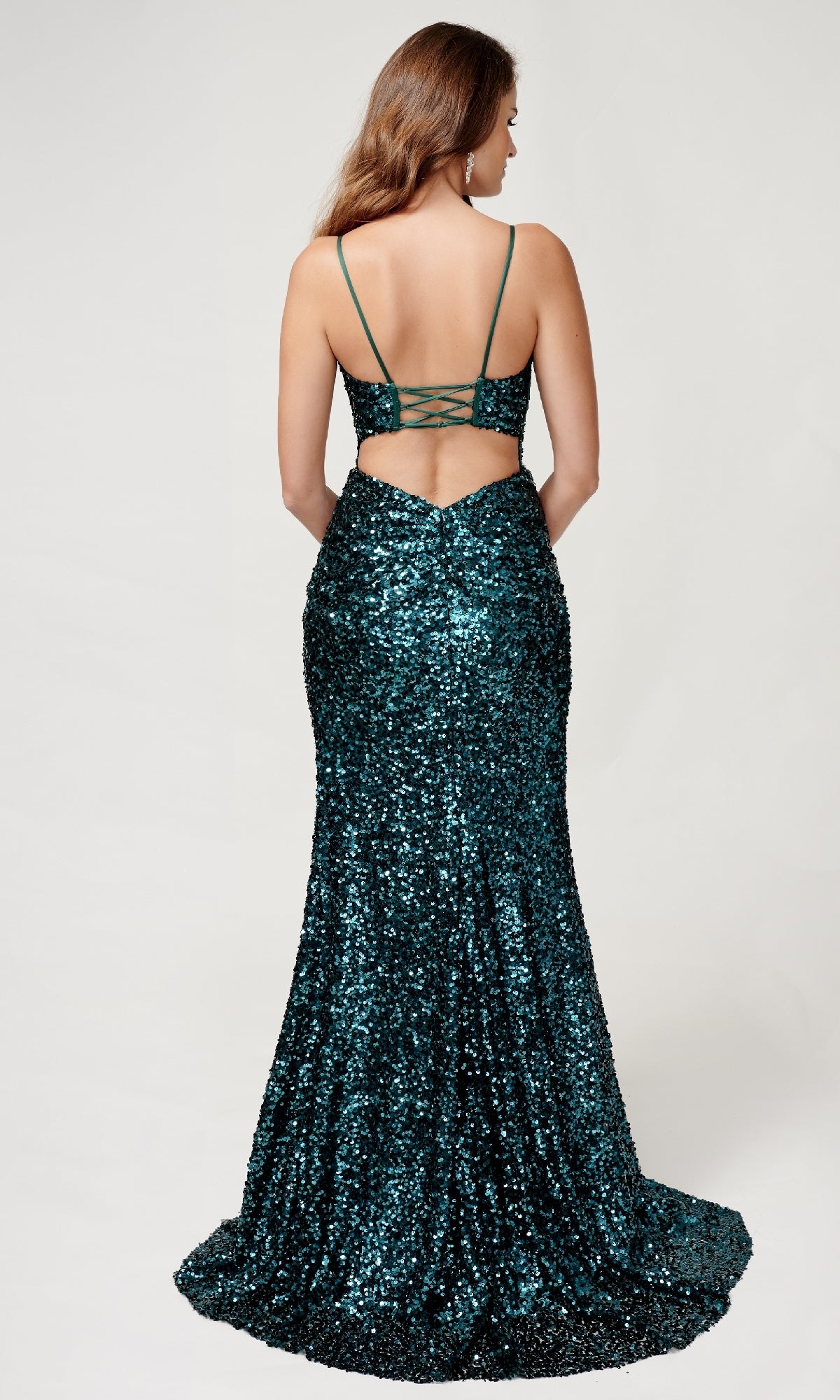 A woman models the Nina Canacci 4406, a floor-length dark green sequin formal dress featuring thin straps, a lace-up back, and a subtle side leg slit, standing against a plain background.